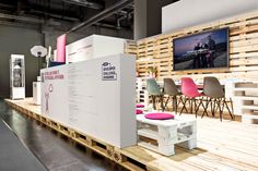 an exhibit room with wooden pallets and white furniture on the floor, along with pink cushions