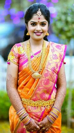 a woman in an orange and pink sari with gold jewelry on her neck, standing outside