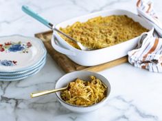 a casserole dish with noodles in it on a wooden tray and plates next to it