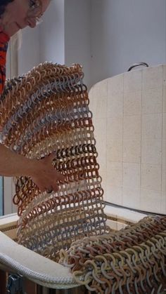 a woman in an orange shirt is working on a piece of furniture made out of chains