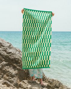 a woman standing on top of a rock next to the ocean holding a green and white scarf