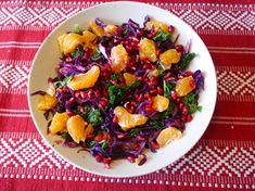 a white bowl filled with oranges, cabbage and pomegranate on top of a red table cloth