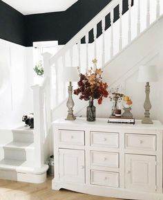 a white dresser sitting under a stair case next to a bannister filled with flowers