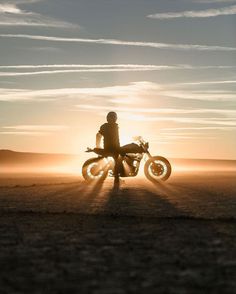 a person on a motorcycle in the middle of nowhere with sun shining through the clouds