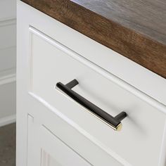 a close up of a drawer handle on a white cabinet with wood top and drawers