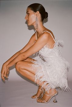 a woman sitting on the ground with her legs crossed wearing high heels and a white feathered dress