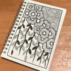 a spiral notebook with flowers and swirls drawn on it sitting on a wooden table