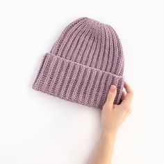 a hand holding up a purple knitted beanie on a white background with copy space