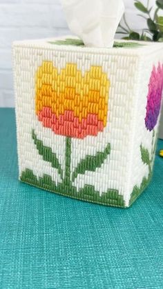 a tissue box decorated with flowers and leaves on a blue surface next to a potted plant