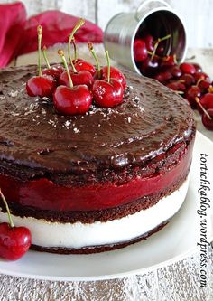 a chocolate cake topped with cherries on top of a white plate next to fresh cherries