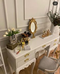 a white desk topped with a mirror next to a chair and vase filled with flowers