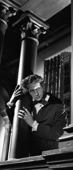 a man in a tuxedo leaning against a pillar with his hands on his head