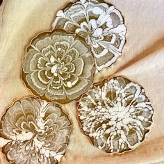 three decorative plates sitting on top of a cloth covered tablecloth with flowers painted on them