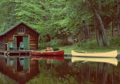 a red boat sitting next to a wooden cabin on top of a lake in the woods