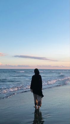 a person walking on the beach with their back to the camera, looking out at the ocean