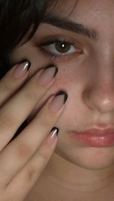 a woman with black and white nail polish holding her hands up to her face while looking at the camera