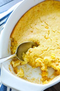 a spoon in a casserole dish with cornbread on the side and a blue towel behind it