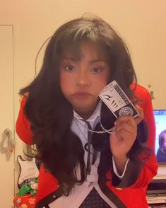 a girl with long black hair wearing a red jacket and white shirt holding up a cell phone in front of her face