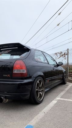 the back end of a black car parked in a parking lot next to power lines