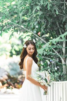 a woman standing next to a white fence holding a bouquet in her hand and looking at the camera