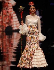 a woman is walking down the runway with a flower in her hand