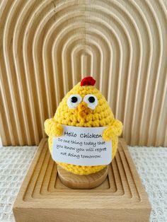 a crocheted chicken holding a sign in front of a wooden box with the words hello chickens written on it