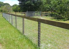 the fence is made of metal wire and has grass growing on it, along with some trees in the background