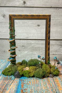 a moss covered frame sitting on top of a wooden table next to rocks and mushrooms