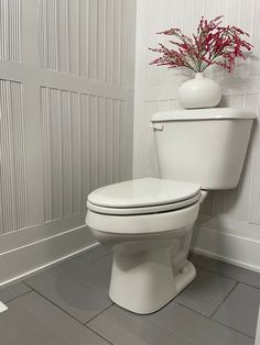 a white toilet sitting in a bathroom next to a vase with red flowers on it