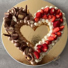 a heart shaped cake with strawberries and chocolates on the top, sitting on a gold plate