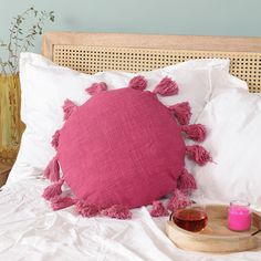 a pink pillow sitting on top of a white bed next to a tray with drinks