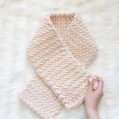 a hand holding a knitted dishcloth on top of a white fur covered floor