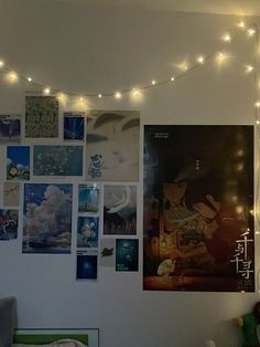 there are many pictures on the wall with lights strung above them and below it is a bed