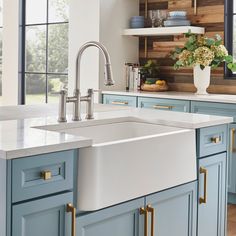 a white kitchen sink sitting under a window next to blue cabinets and counter tops with gold handles