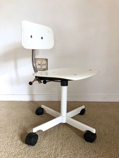 a white desk chair with wheels on the floor in front of a wall and carpet