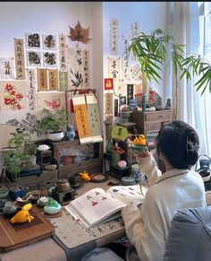 a woman sitting at a desk with an open book in front of her and lots of pictures on the wall behind her