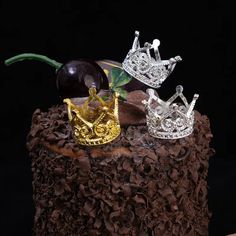 two silver crowns sitting on top of a piece of chocolate cake next to cherries