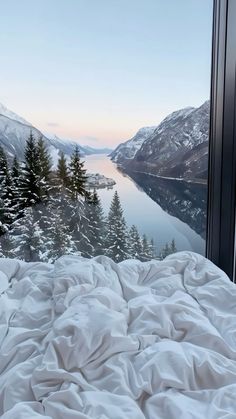 a bed with a white comforter sitting in front of a window overlooking a lake