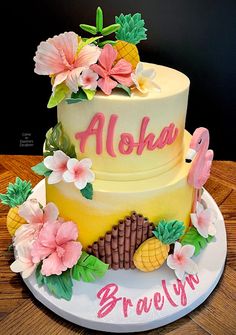 a three tiered cake with pineapples and flowers on top, along with the name aloha