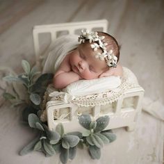 a baby sleeping on top of a white crib next to green plants and leaves