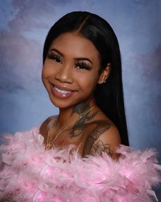 a woman with tattoos and pink feathers on her chest smiling at the camera while posing for a photo