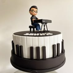 a cake with a man sitting at a piano on it's side and the top tier is black and white