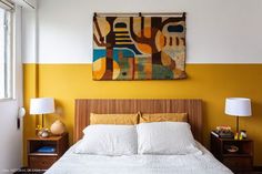 a bed sitting under a painting on the wall next to a lamp and two nightstands