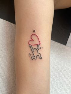 a person with a small tattoo on their arm holding a heart shaped object in the air