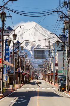 a person walking down an empty street in front of a snow - capped mountain,