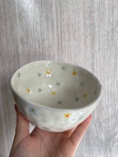 a hand holding a small white bowl with flowers on it