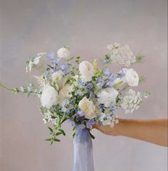 a bouquet of white and blue flowers is being held by a person's hand