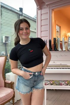 a woman standing in front of a white piano wearing shorts and a black crop top