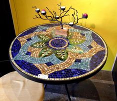 a mosaic table with candles on it and some branches in the center, sitting against a yellow wall