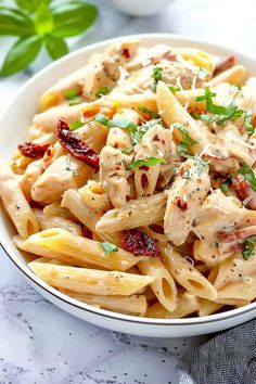 a white bowl filled with pasta covered in chicken and cheese sauce on top of a marble table